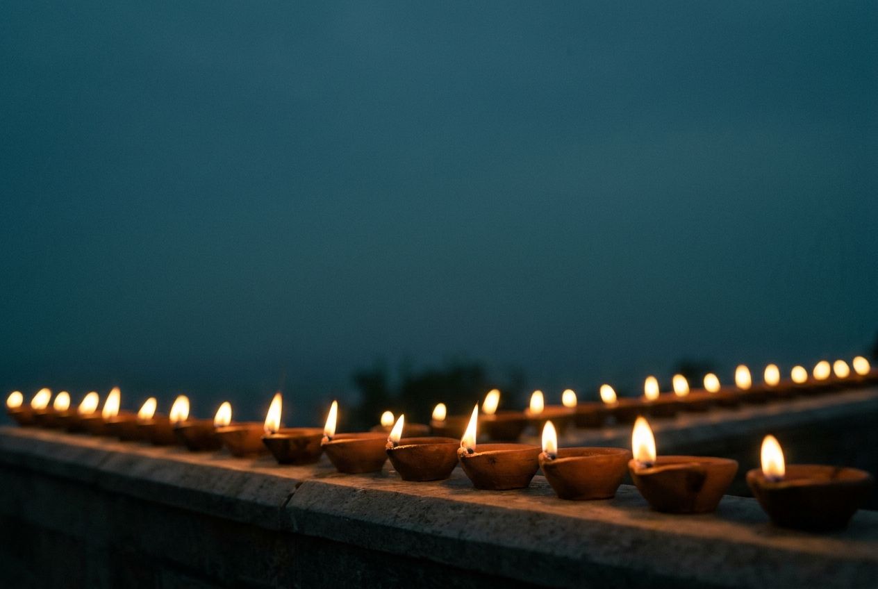 A long row of clay oil lamps lit along a stone ledge at dusk