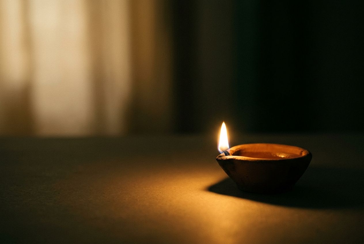 A small clay oil lamp with a single flame glowing in a dark room
